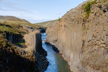 Görkemli bazalt sütunları, Studlagil Kanyonu 'ndan akan parlak mavi nehri çerçeveler, İzlanda' da gün doğumunda açık bir gökyüzü altında doğal güzelliği sersemleten İzlanda özünü yakalar.