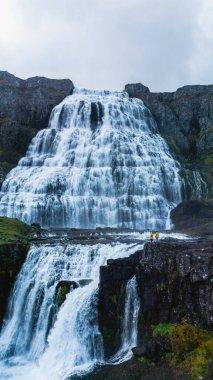 Çarpıcı bir şelale İzlanda 'daki sarp kayalıkların üzerinden zarif bir şekilde dökülür ve sisli bir atmosfer yaratır. Dynjandi Şelalesi, Westfjord, İzlanda