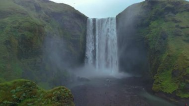 Güçlü Skogafoss şelalesi tarafından büyülenip İzlanda 'nın yemyeşil ve dramatik uçurumlarına düşmek. Sis yükselir, büyüleyici bir atmosfer yaratır ve güzelliği ön plana çıkarır..