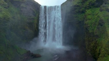 İzlanda 'daki Skogafoss şelalesinin çarpıcı güzelliğini tecrübe edin. Yeşilliğin ortasında 60 metreden zarif bir şekilde akan su nefes kesen doğal bir manzara ve sisli bir atmosfer yaratır..