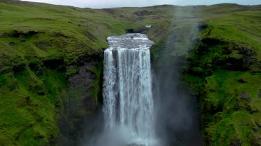 Seljalandsfoss şelalesinin yemyeşil sularla çevrili güçlü bir şekilde akışının muhteşem bir görüntüsü. Sis, yumuşak ışığın altında parıldıyor ve nefes kesici bir manzara yaratıyor..