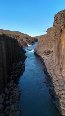 İzlanda 'daki büyüleyici Studlagil Kanyonu' nu keşfedin. Burada eşsiz şekilli bazalt sütunlar canlı mavi bir nehir boyunca dik bir şekilde yükselir. Bu doğal harikanın görkemli güzelliğini tecrübe et..