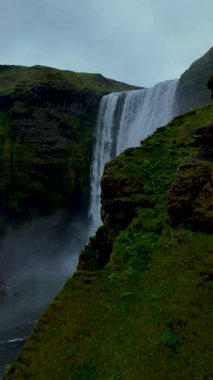 Skogafoss şelalesinin nefes kesici güzelliğini, İzlanda 'daki yosun kaplı kayalıklardan aşağı düşüşünü deneyimleyin. Suyun dingin sesi, bereketli çevrenin güzelliğiyle karışıyor..