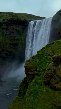 Skogafoss Şelalesinin dalgalı yeşil tepelerle çevrili kayalık uçurumlardan aşağı yuvarlandığını hissedin.