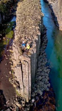 İki kaşif, Studlagil Kanyonu 'ndaki bazalt sütunlardan nefes kesen manzaranın keyfini çıkarıyorlar. İzlanda' daki çarpıcı oluşumlara ve aşağıdaki canlı nehre hayret ediyorlar.