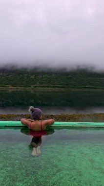 Bir kadın, sakin suların çarpıcı dağ manzaralarıyla buluştuğu İzlanda 'daki jeotermal bir kaplıcada dinleniyor. Rahatlamak için mükemmel bir kaçış, Sıcak havuz, Westfjords, İzlanda