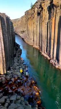 Ziyaretçiler, İzlanda 'daki Studlagil Kanyonu' nun turkuaz sularını kaplayan şaşırtıcı bazalt sütunlara hayret ediyorlar. Bu büyüleyici mekan, doğanın sanatsal yapısını mükemmel bir uyum içinde sergiliyor..