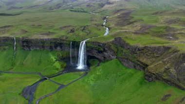 Seljalandsfoss şelalesinin engebeli bir uçurumdan canlı yeşil vadilere düşüşünü izleyin. İzlanda 'nın huzurlu manzarasında güç ve güzelliğe tanık olun..