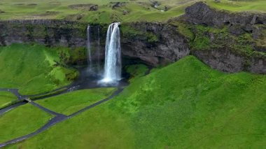 İzlanda 'nın canlı yeşil tepelerine kurulmuş çarpıcı Seljalandsfoss şelalesini keşfedin. Su, dramatik bir şekilde çağlayarak doğa severler ve maceracılar için ideal bir manzara yaratır..