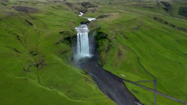 Skogafoss Şelalesi 'nin çarpıcı manzarasının tadını çıkarın. İzlanda' nın yemyeşil tepelerinin ortasındaki kayalık kayalıklardan suyla çarpıcı bir şekilde düşüyor. Bu nefes kesen yerin doğal güzelliğini yakalıyor..
