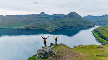 İki yürüyüşçü, şafak vakti Faroe Adaları 'nın dingin sularına ve büyüleyici manzaralarına tepeden bakan büyüleyici Gonguturur Hvithamar Patikası' nda maceralarını kutluyor..