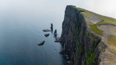 Dik bazalt kayalıklar, sakin suların üzerinde, Faroe Adaları 'nın engebeli güzelliğini gözler önüne seriyor. Risin OG Kellingin uçurumları