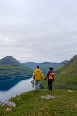 İki yürüyüşçü, Faroe Adaları 'nın göz kamaştırıcı manzaralarını gören Gonguturur Hvithamar Patikası boyunca el ele yürürler. Yeşillik yeşil tepeler aşağıda sakin sularla buluşur ve sakin bir kaçış yaratır..