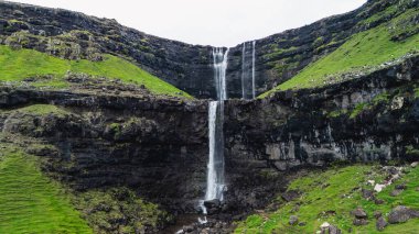 Faroe Adaları 'nın çarpıcı manzarasındaki yüksek uçurumlardan zarif bir şekilde su taşar. Fossa şelalesi