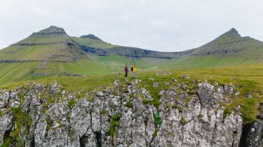 İki yürüyüşçü etkileyici Gonguturur Hvithamar Patikası 'nı geçer, dramatik uçurumlar ve verimli yeşil manzaralarla çevrili, tipik Faroe Adaları' nın tipik, sakin, bulutlu gökyüzü altında..