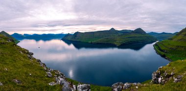 Gonguturur Hvithamar Patikası boyunca Faroe Adaları 'nın nefes kesici manzaralarını keşfedin. Sakin sular engebeli tepeleri yansıtıyor, alacakaranlık sırasında büyüleyici bir atmosfer yaratıyor..