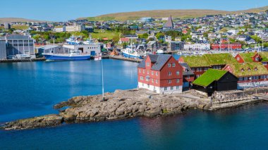 Torshavn, resim gibi limanı boyunca canlı kırmızı ve yeşil mimariler sergiliyor. Yelkenliler ve balıkçı tekneleri açık mavi gökyüzünün altındaki yemyeşil tepelere karşı suları süsler..