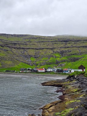 Tjornuvik köyü, engebeli kıyı şeridi boyunca çeşitli renklerde geleneksel evlerin yer aldığı Faroe Adaları 'nın dramatik uçurumlarına karşı kurulmuştur..