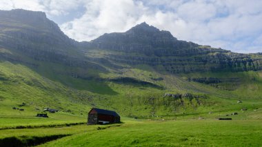 Faroe Adaları 'ndaki sakin bir ortamda yemyeşil kayalıklar çarpıcı bir şekilde yemyeşil manzaranın üzerinde yükseliyor. Kallur Deniz Feneri, Kalsoy Adası