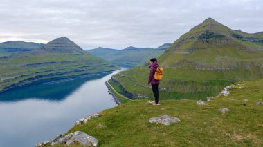 Yürüyüşçü, Faroe Adaları 'nın canlı yeşil tepeleri ve sakin suları ile çevrili Gonguturur Hvithamar Patikası boyunca nefes kesici manzaranın tadını çıkarmaktadır. Doğada sakin bir macera.