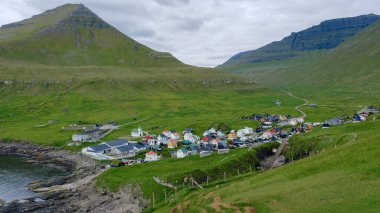 Gjogv köyü, yüksek yeşil tepeler ve Faroe Adaları 'ndaki engebeli uçurumlar arasında kurulmuş kıyı şeridi boyunca canlı evler ortaya çıkarıyor..