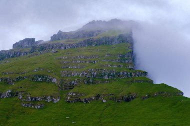 Yükselen uçurumlar yemyeşil tepelerden dramatik bir şekilde yükseliyor, kısmen dönen sisle örtülü. Bu nefes kesici manzara, Kalsoya 'nın engebeli arazisinin özünü yakalar.