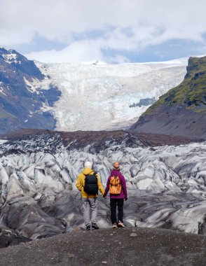 Yürüyüşçüler İzlanda 'daki Svinafellsjokull Buzulu' na hayret ediyorlar. Yüksek buz oluşumları ve engebeli arazi kaşifler doğanın güzelliğini tecrübe ettikçe çarpıcı bir zemin oluşturur..