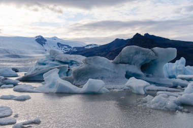 Işıldayan buzdağları İzlanda 'da dramatik dağlarla çevrili sakin bir buzul gölünde huzur içinde yüzer..
