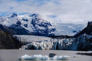 Görkemli Svinafellsjokull Buzulu dramatik bir gökyüzünün altında karmaşık buz oluşumları ve yüksek zirveler sergiliyor. Huzurlu manzara, İzlanda 'nın kalbine keşif ve macera davet ediyor..
