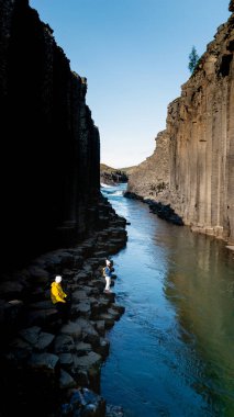 Studlagil Kanyonu 'nun doğal güzelliği, maceraperestlerin kristal berrak sularda kayalıklarda gezinmesiyle sergilenir. Yükselen bazalt sütunlar dramatik bir şekilde yükselir, huzurlu nehri çerçeveler..