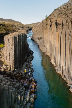 İzlanda 'daki Studlagil Kanyonu, sakin bir turkuaz nehrin kıyısında dik duran geometrik bazalt sütunları sergiliyor. Maceracılar kanyonları keşfederler Bu büyüleyici manzarada kayalık kıyıları.