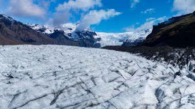 İzlanda 'daki Svinafellsjokull Buzulu' nun çarpıcı manzarası, kar kaplı dağlar ve canlı mavi gökyüzü ile buz dokusunu vurguluyor..
