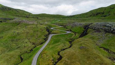 Dönek bir yol, Faroe Adaları 'nın yemyeşil tepelerinde, dramatik manzaralarla çevrili..