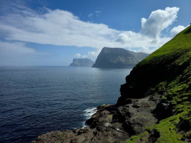 Sakin suların üzerinde nefes kesici uçurumlar yükselir ve Faroe Adalarının doğal güzelliklerini gözler önüne serer. Bereketli yeşil yamaçlar kayalık kıyı şeritleriyle buluşur, açık bir günde güzel bir manzara sunar..