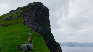Yürüyüşçülerin dramatik uçurumların yanındaki yemyeşil yamaçlardan geçerken Faroe Adaları 'nın nefes kesici güzelliğini tecrübe edin. Kallur Deniz Feneri Kalsoy Adası