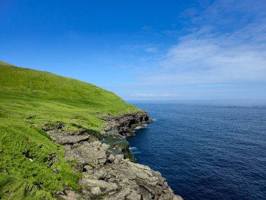 Bereketli yeşil tepeler, Faroe Adaları 'nın engebeli kıyı şeridi boyunca uzanan derin mavi sularla karşılaşıyor. Parlak bir gökyüzünün altında, dokunulmamış güzellikleri ve dinginliği gözler önüne seriyor..