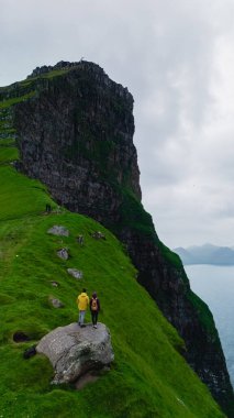 Faroe Adaları 'nın turkuaz sularından heybetli uçurumlar yükselir. Bir çift birlikte duruyor, hayranlık uyandıran manzaralarda, Kallur Deniz Feneri Kalsoy Adası