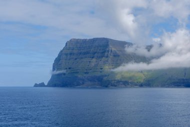 Faroe Adaları 'nın sakin sulardan yükselen nefes kesici uçurumlarını keşfedin. Yeşillik ve gizemli bulutlar büyüleyici bir atmosfer yaratıyor, Kalsoy Adası.