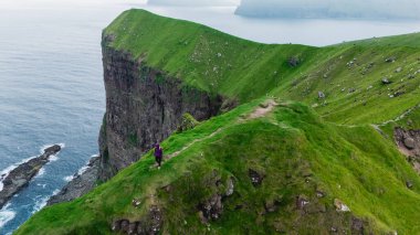 Faroe Adaları 'ndaki Atlantik Okyanusu' ndan dramatik uçurumlar görkemli bir şekilde yükselir ve manzaranın nefes kesici manzarasını sunar. Yalnız bir figür engebeli araziyi keşfediyor, Kallur Deniz feneri Kalsoy Adası