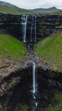 Majestic Fossa şelalesi, canlı yeşil tepelerle çevrili Faroe Adaları 'ndaki kayalık uçurumlara çarpar. Sakin atmosfer ve doğal güzellik büyüleyici bir manzara yaratır..