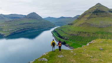 İki yürüyüşçü, Faroe Adaları 'nın nefes kesici fiyortlarına tepeden bakan Gonguturur Hvithamar Patikası' nda el ele durmaktadır..