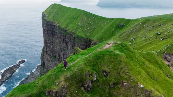 Faroe Adaları 'ndaki Atlantik Okyanusu' ndan dramatik uçurumlar görkemli bir şekilde yükselir ve manzaranın nefes kesici manzarasını sunar. Yalnız bir figür engebeli araziyi keşfediyor, Kallur Deniz feneri Kalsoy Adası