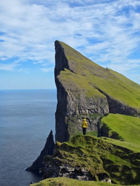 Cesur bir yürüyüşçü Mylingur Tepesi 'nde duruyor, Faroe Adaları' nın nefes kesici sahil şeridine bakıyor. Yeşil uçurumlar engin mavi okyanusla buluşur güzel bir gökyüzünün altında, ilham verici bir macera.