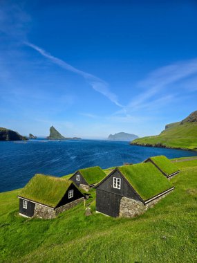 Faroe Adaları 'nın sakin sularına bakan geleneksel otlaklı kulübelerin kırsal cazibesini keşfedin. Canlı yeşil tepeler ve sakin deniz manzaralı bir ortam yaratır. Bour Köyü
