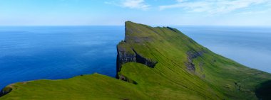 Faroe Adaları 'ndaki Atlantik Okyanusu' ndan görkemli uçurumlar dramatik bir şekilde yükselir. Bereketli yeşil yamaçlar derin mavi denize karşı çarpıcı bir kontrastlık yaratır. Keşif ve maceraya davetiye çıkarır..