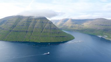 Görkemli yeşil dağlar Faroe Adaları 'nın dingin sularının üzerinde dramatik bir şekilde yükselir..