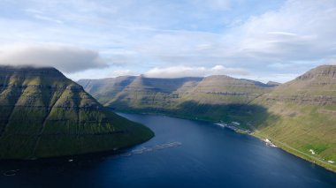 Feroe Adaları 'nın nefes kesen manzarasında dingin fiyortu çevreleyen sarp yeşil tepeler vardır. Güneş ışığı, Klakkur 'un engebeli arazisini aydınlatan dramatik gölgeler bırakıyor. 