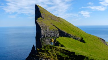 Majestic Mylingur kayalıkları gök mavisi Faroe Adaları 'na çarpıcı bir şekilde yükseliyor. Yalnız bir yürüyüşçü huşu içinde duruyor, baş döndürücü doğal güzelliğin içinde.