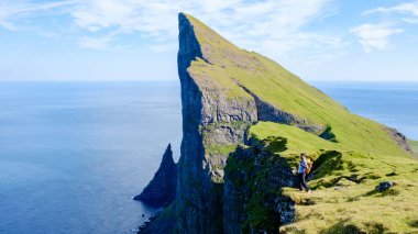 Bir yürüyüşçü, Faroe Adaları 'ndaki Atlantik Okyanusu' na bakan dik bir Mylingur uçurumunun kenarında cesurca duruyor. Çarpıcı manzara, açık gökyüzünün altında yemyeşil ve kayalık oluşumlar sergiliyor..
