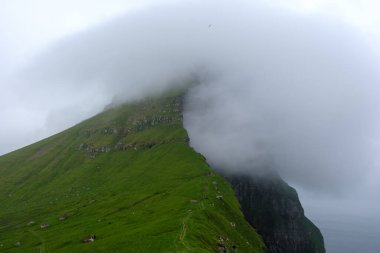 Faroe Adaları 'ndaki denizden yükselen görkemli uçurumlar yumuşak, dönen sisle kaplıdır. Kallur Deniz Feneri, Kalsoy Adası